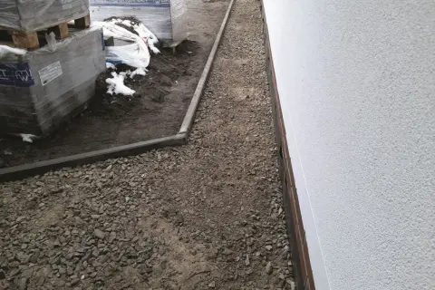 Gotowy do układania kostki brukowej: warstwa podsypki pod kostkę, obrzeża i palety z materiałem budowlanym.
