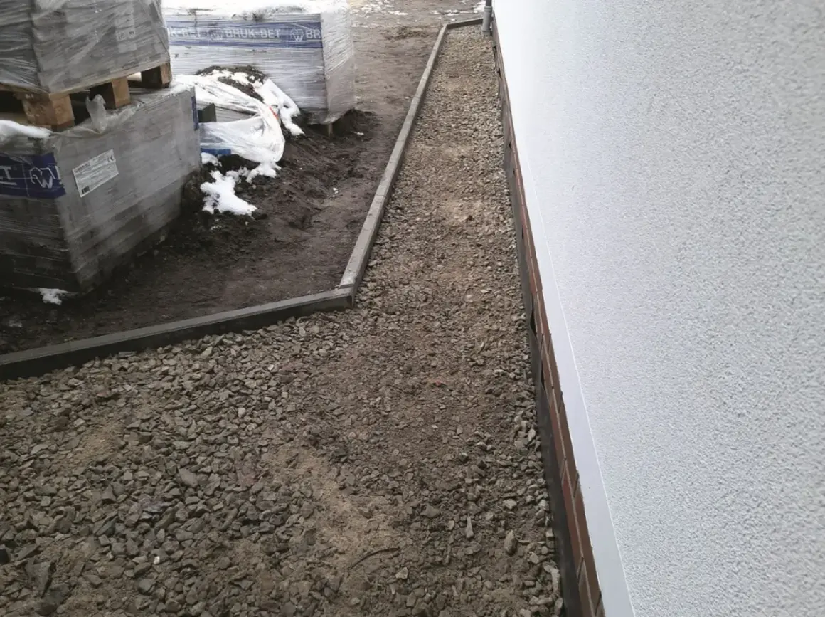 Gotowy do układania kostki brukowej: warstwa podsypki pod kostkę, obrzeża i palety z materiałem budowlanym.