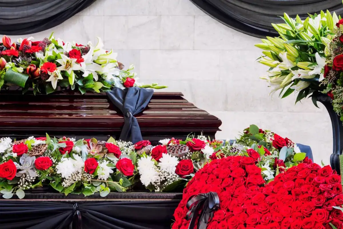 Trumna ozdobiona bukietami czerwonych róż i białych lilii. Kwiaty po pogrzebie symbolizują pamięć i żal, a ich obecność przez 6 tygodni to czas refleksji.